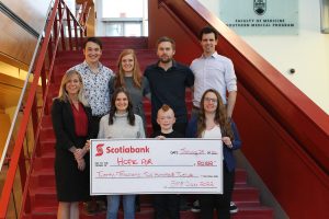 Southern Medical Program students (L-R) Brendan Lim, Talia Del Medico, Brianna Creelman, Conor Barrie, Allyssa Hooper, and Brayden Fishbook along with Scotiabank Business Advisor Christy St. Jean present a cheque to Hope Air patient ambassador Ty.
